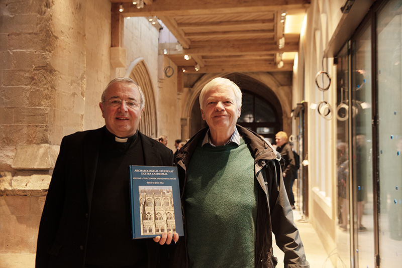 The photo shows Exeter Cathedral Archaeologist John Allan holding a copy of his new book, standing next to the Very Rev'd Johnathan Greener, Dean of Exeter. Both are standing in Exeter Cathedral's new Friends Cloister Gallery.